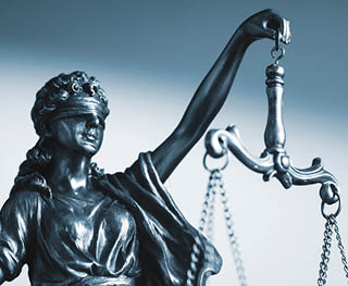 Blindfolded figure of Justice holding scales and a sword conceptual of the courts, judgement, law and order in a beam of light over a grey background with copy space