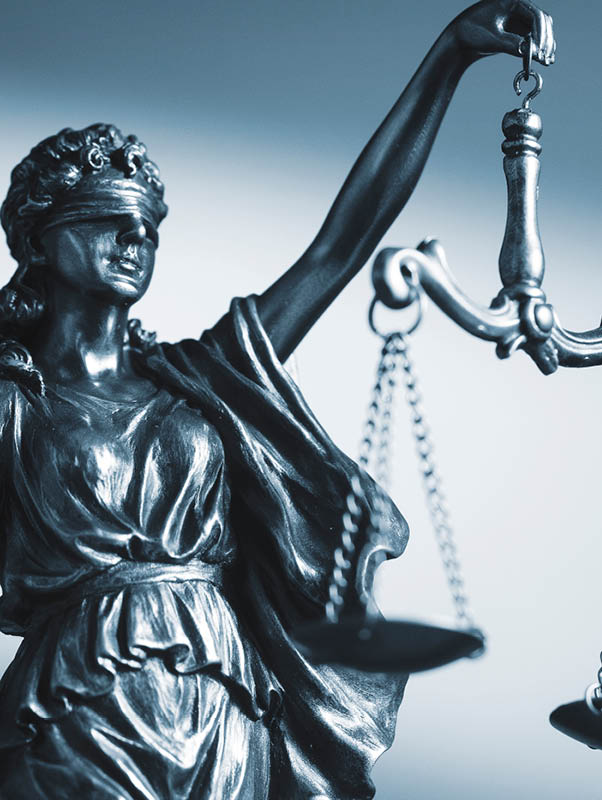 Blindfolded figure of Justice holding scales and a sword conceptual of the courts, judgement, law and order in a beam of light over a grey background with copy space